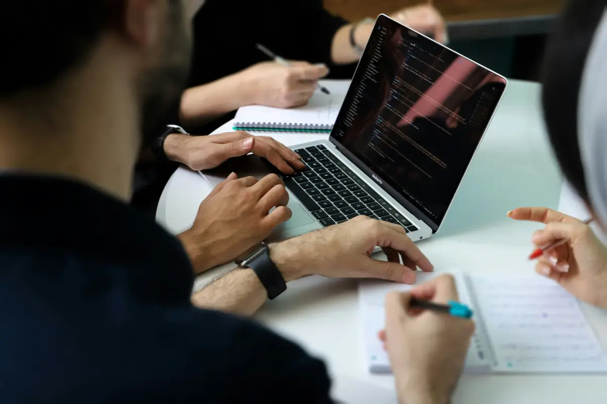 Hands on a laptop keyboard and a notebook during a working session at a white table.