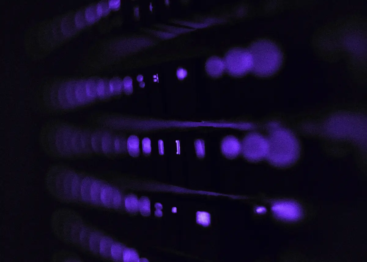Close-up of server rack status lights glowing violet in a dark room.